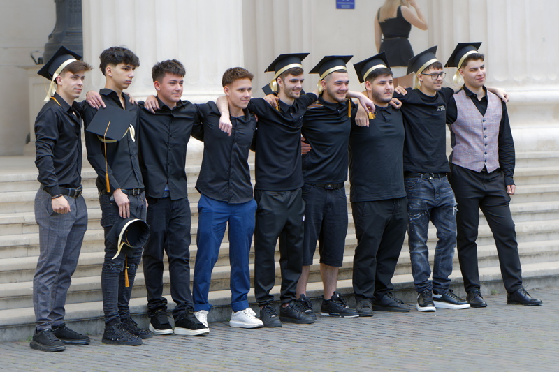 Group of young men in black shirts and graduation caps posing together